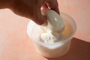 A view of a hand lifting up burrata cheese from a container.