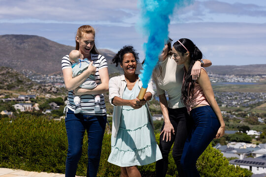 Group of diverse female friends celebrating boy gender reveal with blue smoke, smiling and joyful