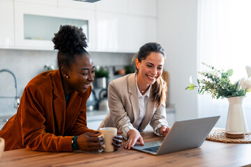 Caucasian and Black Women Collaborate Remotely in Bright Kitchen with Laptops