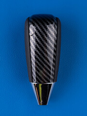 close-up of black automatic transmission gear knob with carbon insert on blue background