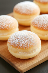 filled donuts with powdered sugar dusting displayed on wooden serving board for bakery treats