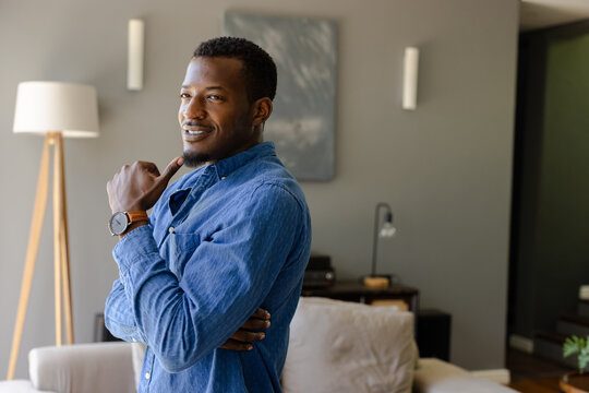 Smiling confidently, man in denim shirt sitting thoughtfully at home