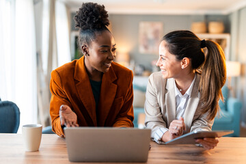 Diverse Business Women Collaborate Over Laptop In Modern Home Office With Natural Light And Warm...