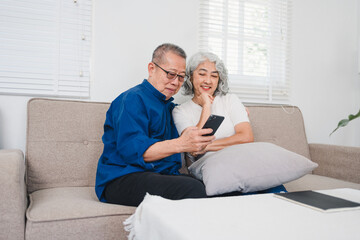 Happy senior couple sitting on sofa looking at smartphone, discussing pension savings and enjoying their time together.