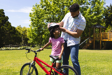 Fototapeta premium Father adjusting daughter's helmet while she prepares to ride bicycle in park
