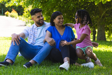Fototapeta premium Smiling family sitting on grass in park, enjoying sunny day together