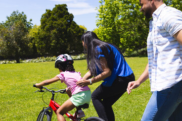 Fototapeta premium Family teaching daughter to ride bicycle in sunny park, enjoying outdoor activity