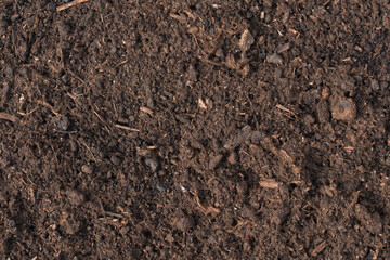 Close-up of rich, dark soil with organic matter and small particles, perfect for gardening, agriculture, and environmental themes. The detailed texture showcases natural elements