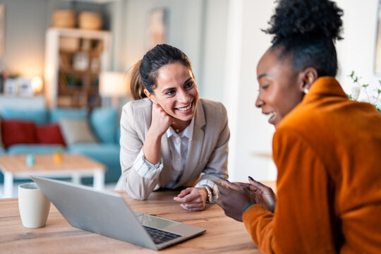 Two Diverse Business Women Having Productive Discussion Over Laptop In Naturally Lit Home Office Space