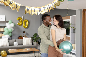 Celebrating 30th birthday with balloons, African American man and woman smiling at home