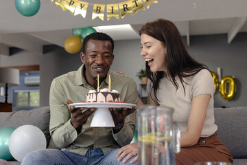 Joyful Diverse couple celebrating birthday with cake and candles in cozy living room