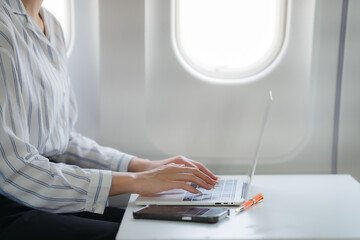 Working in Transit: A person focused on their laptop in an airplane, using mobile devices and connecting with window as background. 