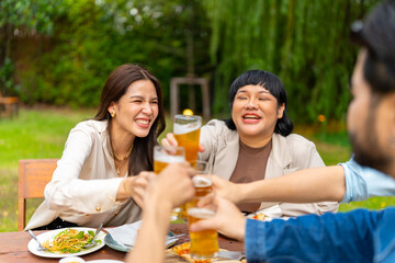 Group of Happy Asian millennial generation people friends enjoy and fun toasting beer glasses celebration reunion meeting at outdoor dinner party in the garden at restaurant on holiday vacation.