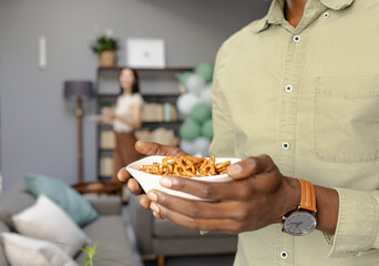 African American man holding bowl of pretzels at home celebration, smiling
