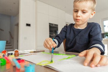 boy draws with acrylic paint on a sheet of paper, a boy of European appearance 4-5 years old draws with paints at home
