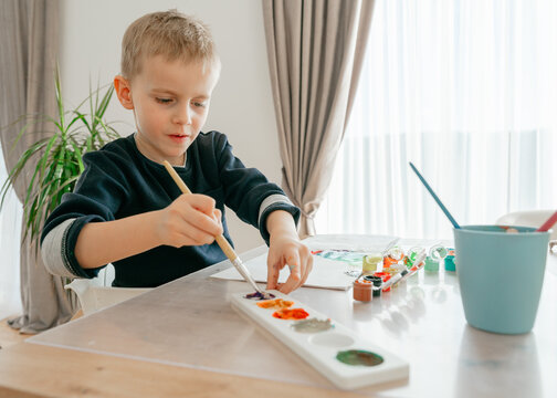boy mixes paints in a palette, a boy of European appearance 4-5 years old paints with paints at home