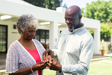 Senior diverse senior couple exchanging rings in garden, celebrating love and commitment together