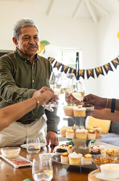 Senior diverse friends toasting with wine glasses around cupcake tower at birthday, at home