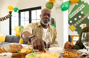 African American Senior man enjoying retirement party, reaching for snacks at festive table, at home
