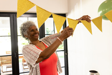 Senior woman decorating home with yellow bunting, smiling joyfully