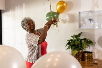 Senior woman decorating with balloons at home, preparing for celebration