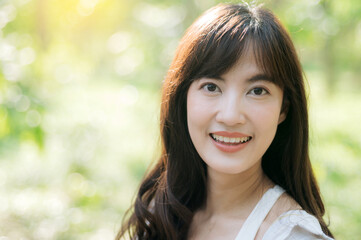 Naklejka premium Asian woman enjoying summer outdoors, breathing fresh air with cheerful smile in lush green park under warm sunlight