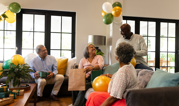 Celebrating birthday at home, diverse senior friends exchanging gifts and having joyful conversation