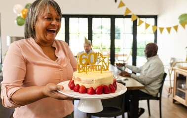 Senior woman holding birthday cake with 60th topper, smiling joyfully, at home