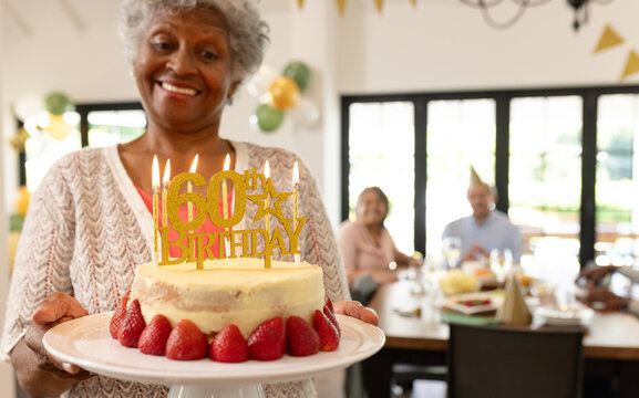 Smiling at diverse senior friends party, woman holding cake with candles, at home