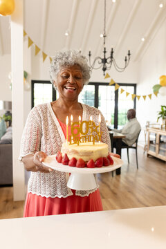 Senior woman celebrating birthday holding cake with candles and smiling joyfully, at home