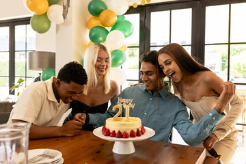 Diverse friends celebrating 21st birthday with cake, smiling and enjoying party at home