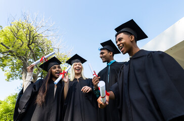 Diverse graduates in caps and gowns celebrating in garden, holding diplomas and smiling