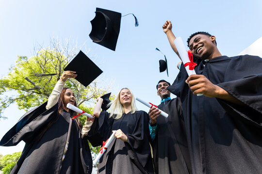 Celebrating graduation, diverse students throwing caps in air, feeling joyful in garden