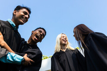 Diverse graduates in gowns celebrating achievements, laughing joyfully in garden, copy space