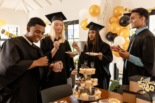 Diverse graduates celebrating with snacks and drinks at home, enjoying their success