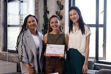 Celebrating achievement, diverse businesswomen holding certificate in modern office