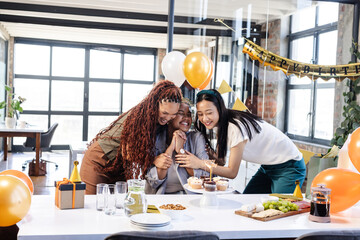 Female diverse colleagues celebrating birthday with cake and gifts in modern office setting