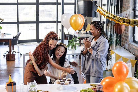 Celebrating birthday at office, female diverse colleagues enjoying cupcakes and balloons