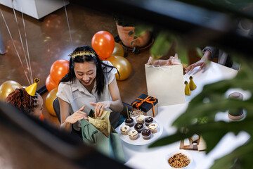 Joyful woman opening gift at office party with cupcakes and balloons