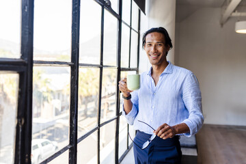 Smiling man holding coffee cup by large office window, enjoying break, copy space