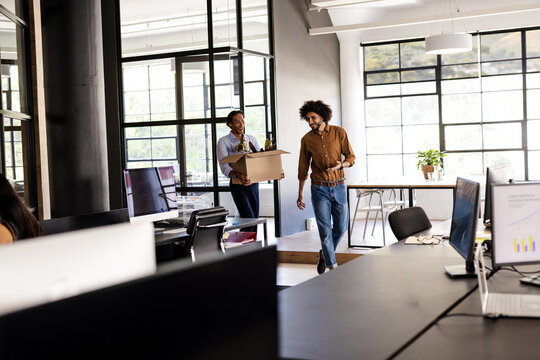 Diverse colleagues carrying box and smiling while moving into modern office space