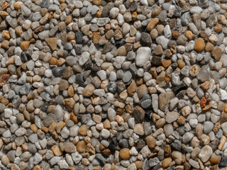Rough Floor Made Of Small Stones Of Various Sizes. Stone Wall Composed Of Tiny White, Brown And Black Stones Embedded In Cement.