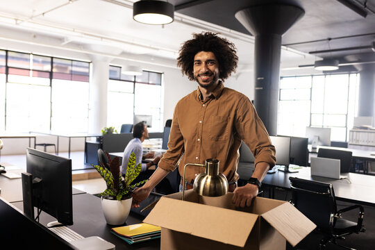 Smiling man unpacking box in modern office, starting new job with enthusiasm