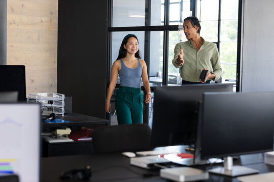 Discussing project, diverse colleagues walking through modern office, smiling and engaged