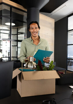 Smiling man unpacking office supplies from box in modern workspace