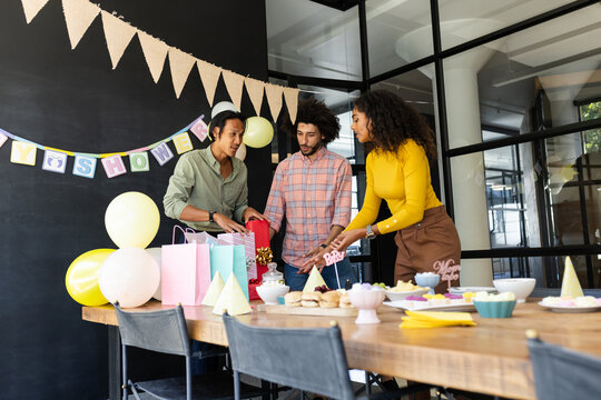 Decorating for baby shower, diverse team arranging gifts and balloons in office
