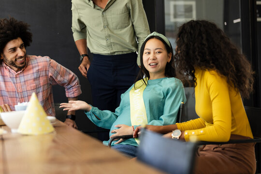 Diverse colleagues celebrating baby shower, smiling and chatting around conference table, at office - Powered by Adobe