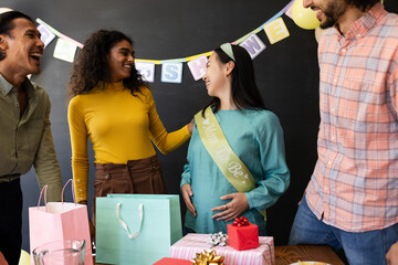 Celebrating baby shower, friends giving gifts and laughing with expectant mother, at office