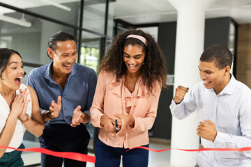 Diverse business team celebrating ribbon cutting ceremony with excitement and joy, at office