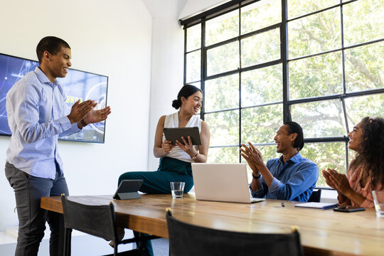 Diverse business team collaborating and applauding during meeting in modern office